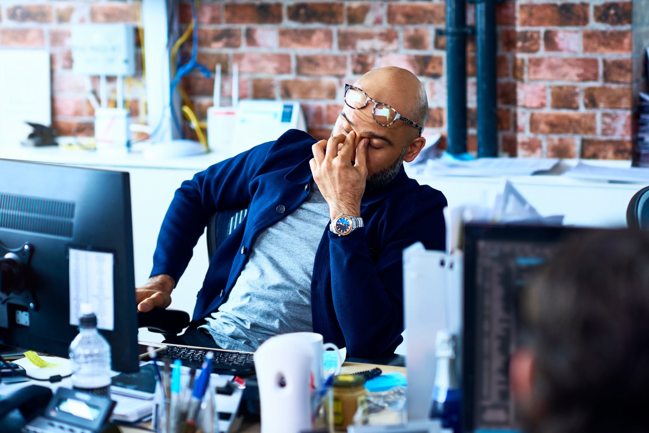 A person at their desk, rubbing their eyes, looking concerned. 