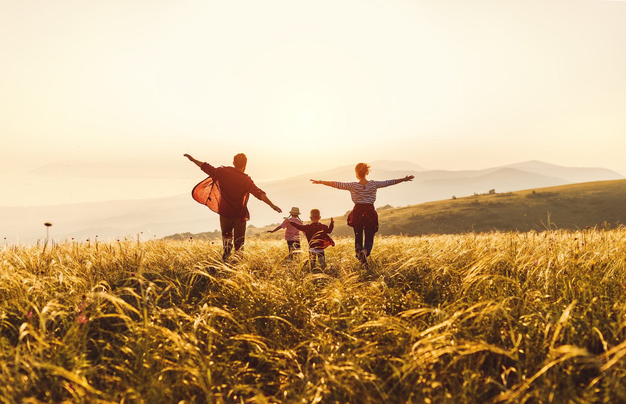 A family running in a field looking at the sunset.