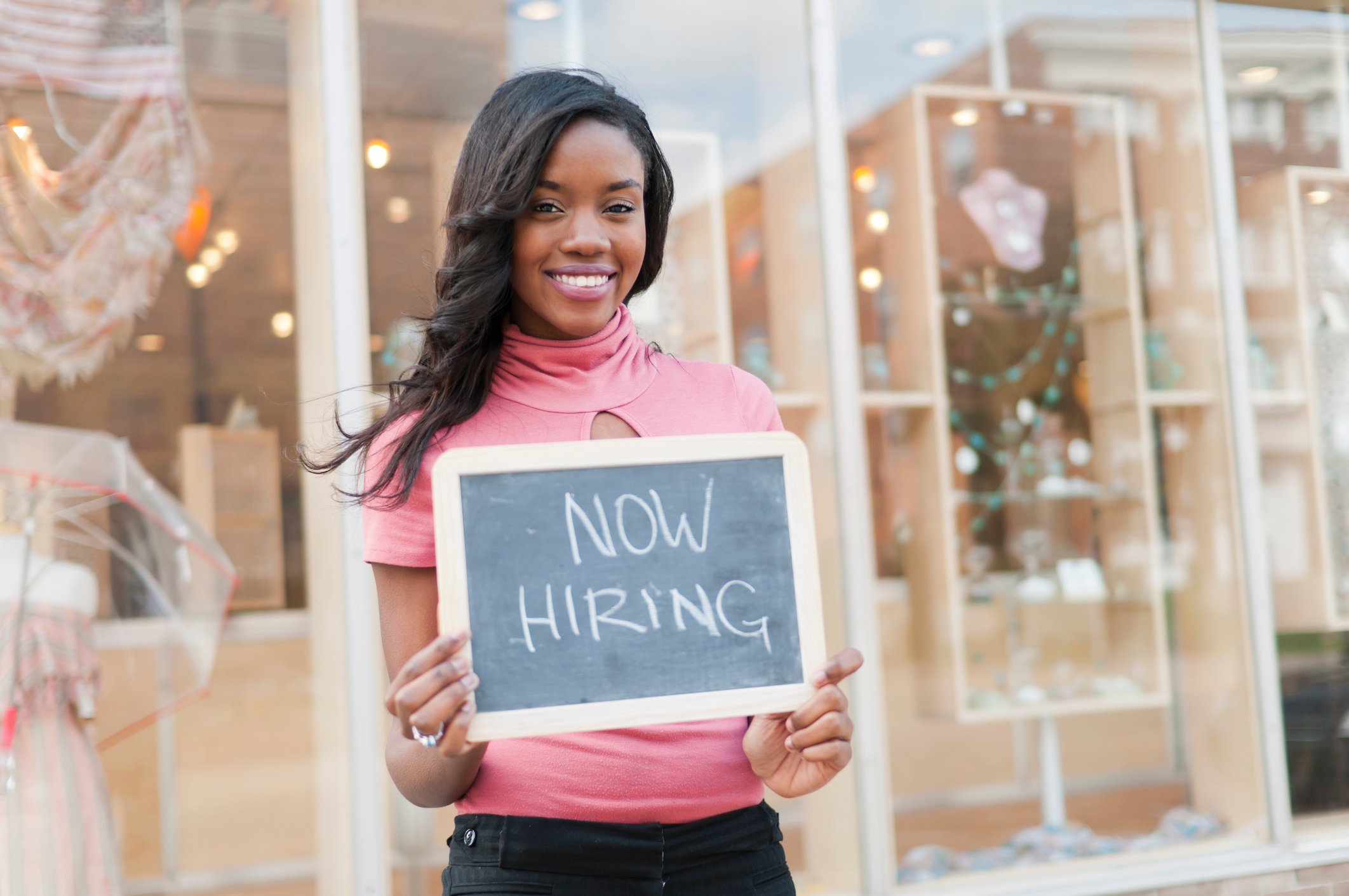 A woman holding up a now hiring sign.