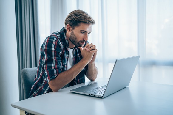 A person sits at a table and looks at a laptop.