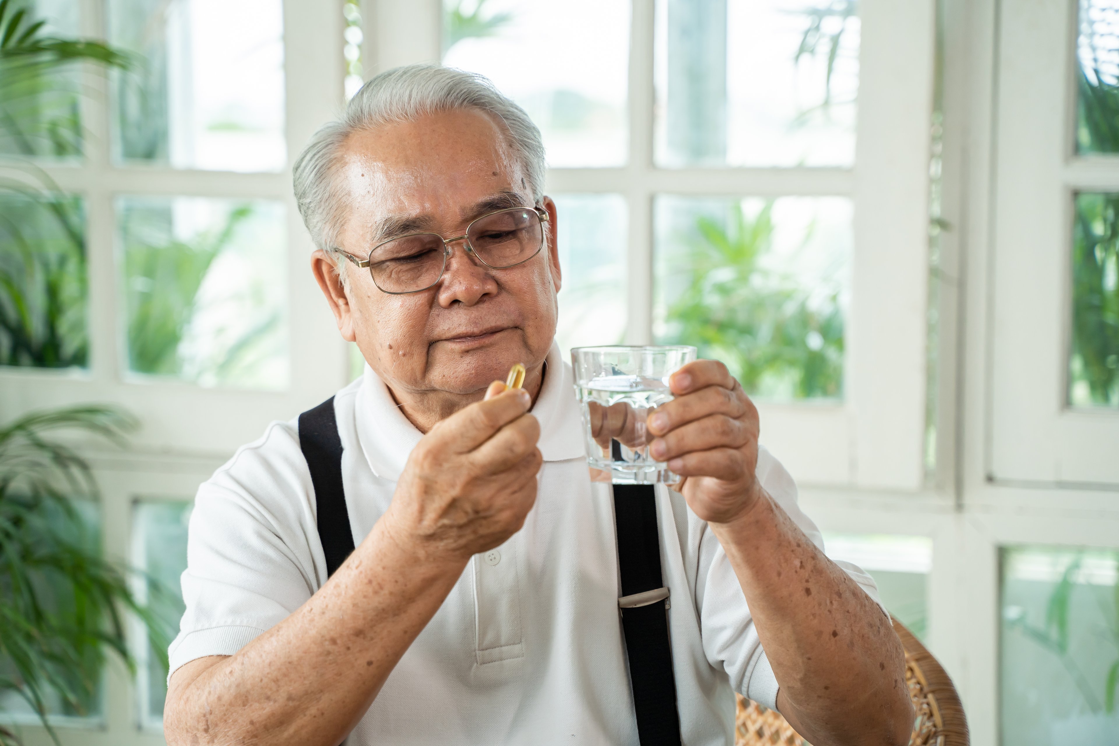 An elderly person taking a fish oil pill. 