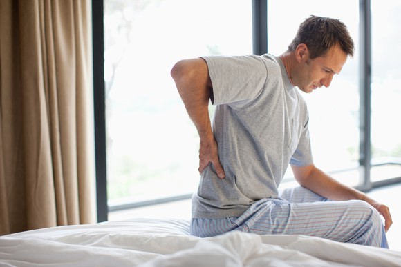A person on a bed clutching their back in pain.