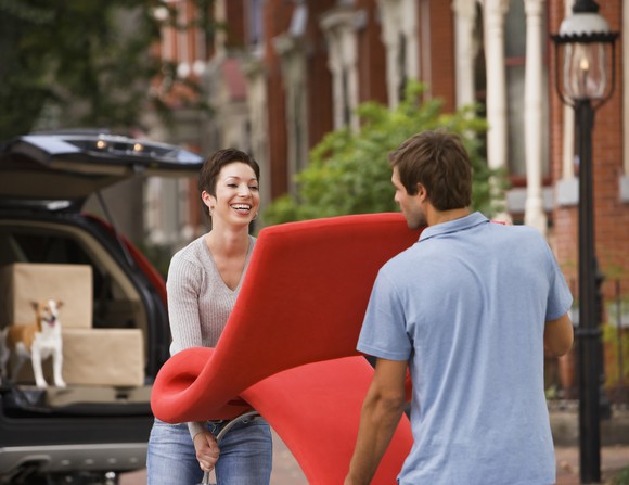Two people moving a chair outside a home.