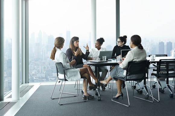 A group of business people sitting around a table in a boardroom overlooking the city.