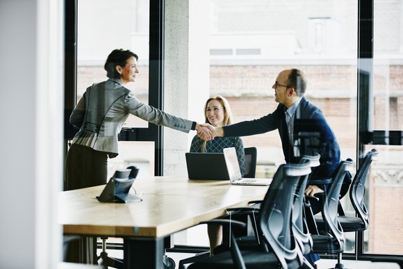 Two business people shake hands in a conference room.