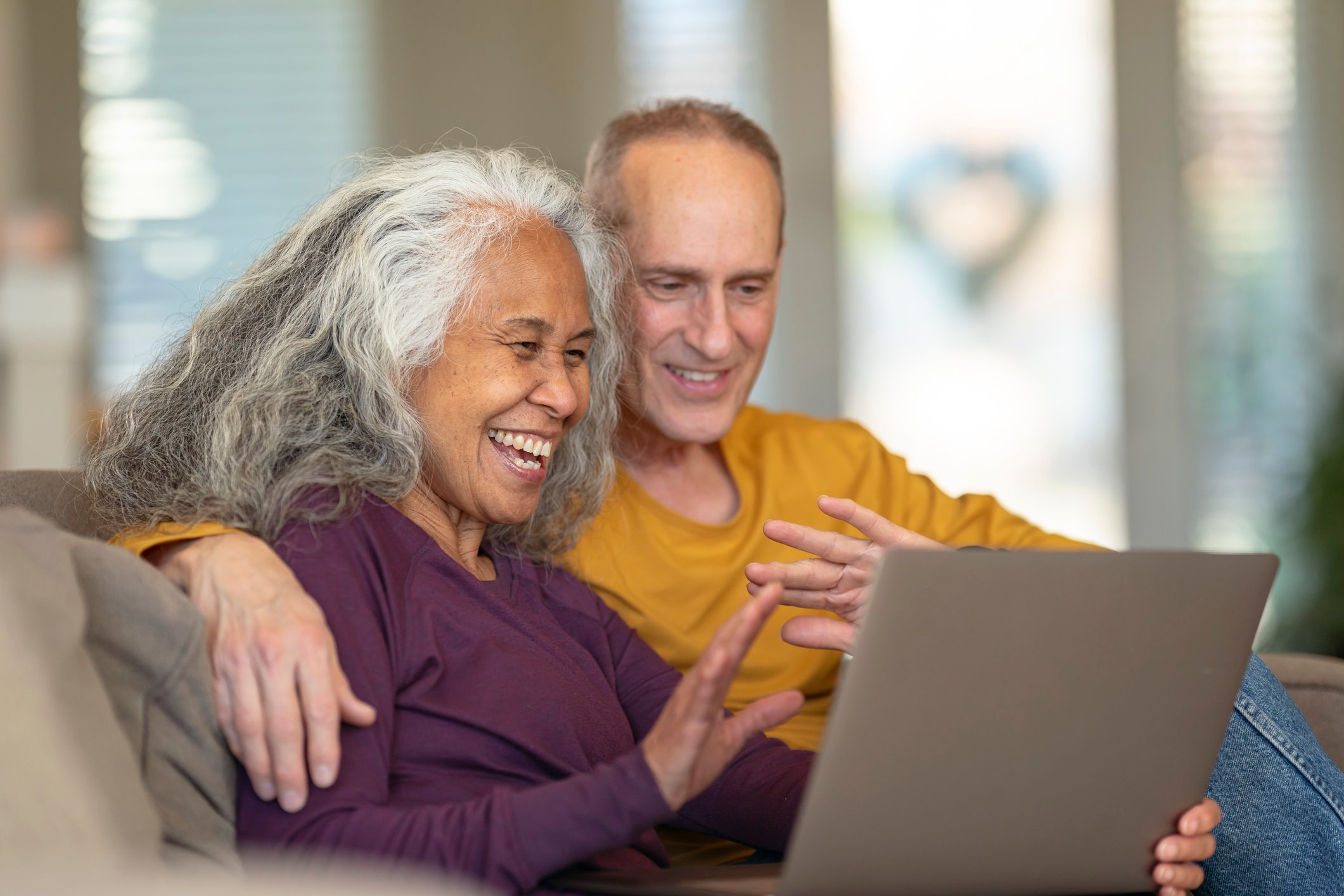 Two people sitting on a couch while looking at an open laptop.