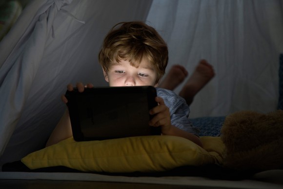 A kid using a tablet in the dark.