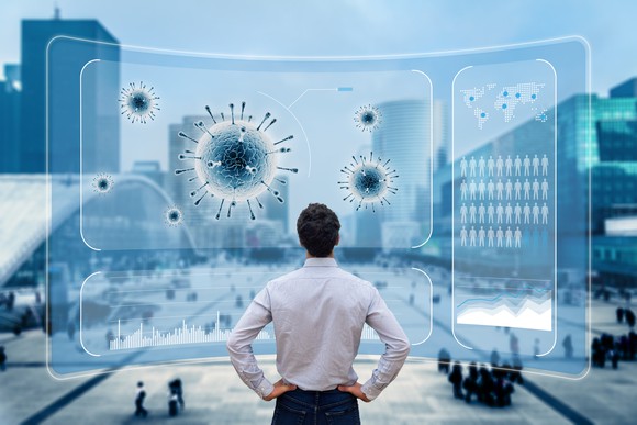 A person looking at a computerized image of the coronavirus and a world map with a city street in the background.
