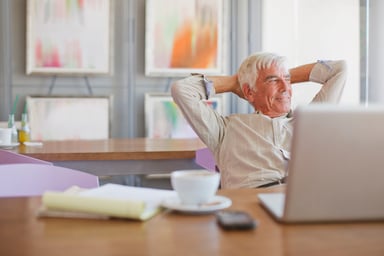 Older man with hands behind his head and laptop