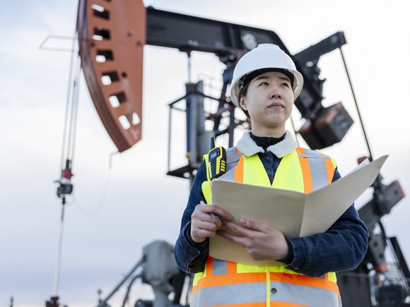 A person holding a folder in front of an oil pumpjack. 