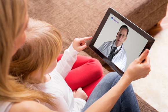 An adult and a child videoconferencing with a medical professional. 