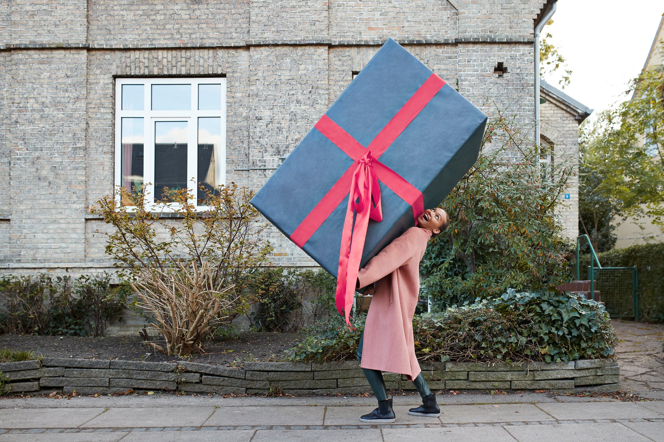 A woman carries a huge gift thats bigger than she down a street. 