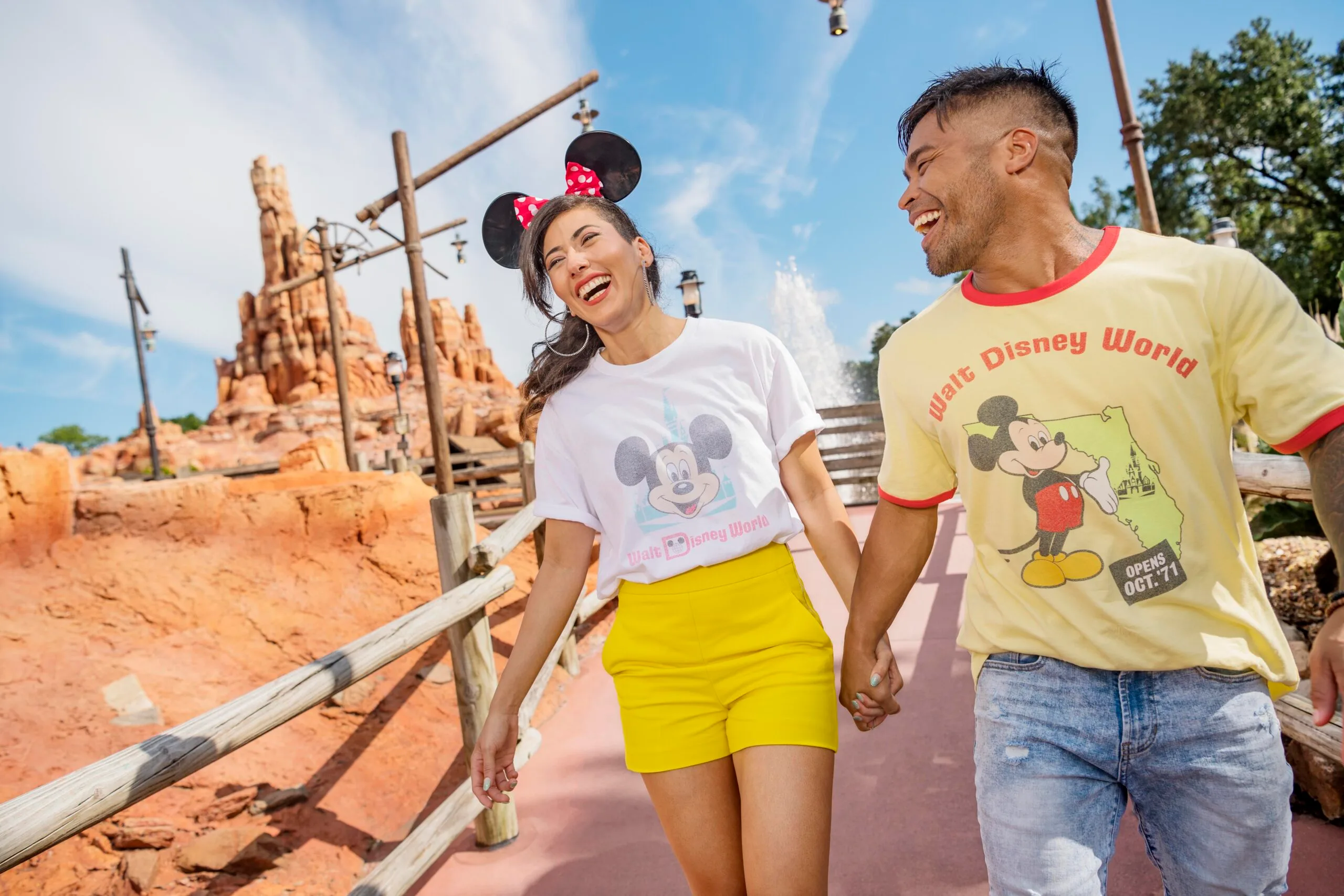 couple walking through Disneyland wearing Mickey Mouse shirts and ears. 