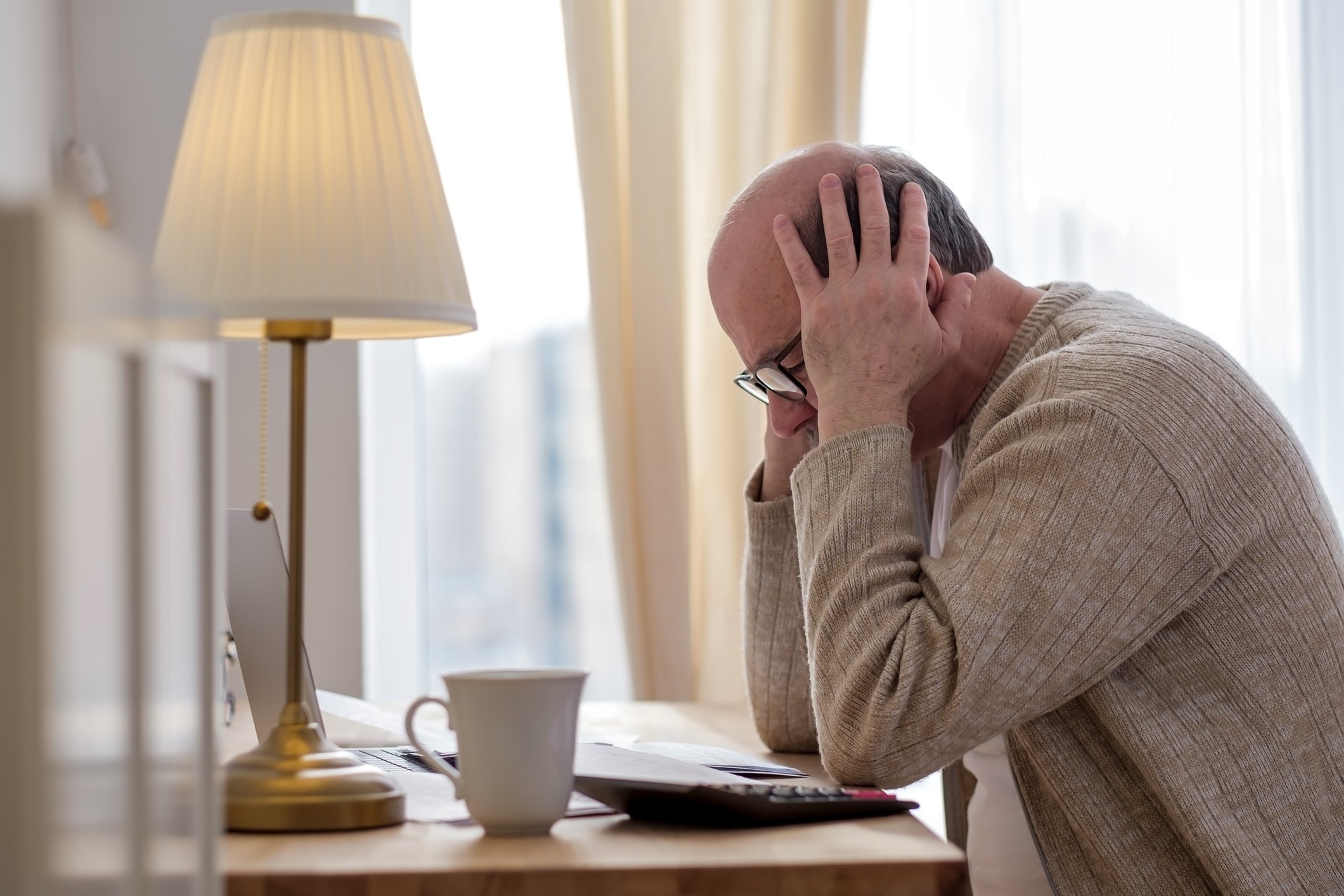Stressed and worried person at desk with hands on head.