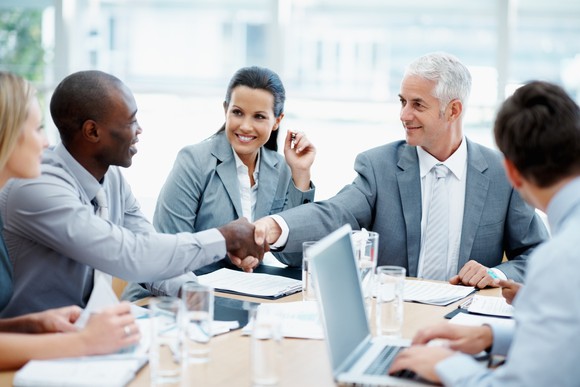Business people shake hands during a board meeting.