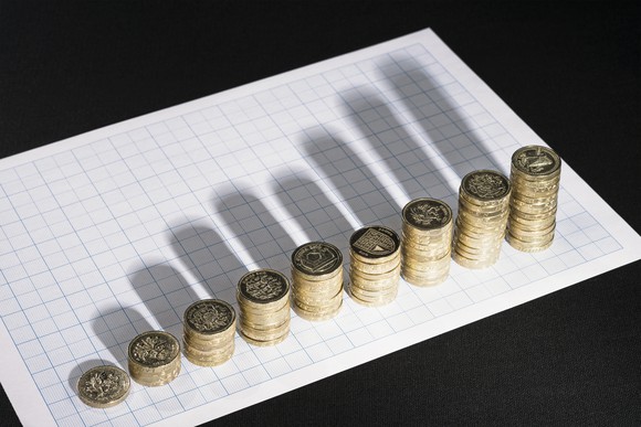 Growing stacks of coins, whose shadows on a piece of paper resemble a financial bar chart.