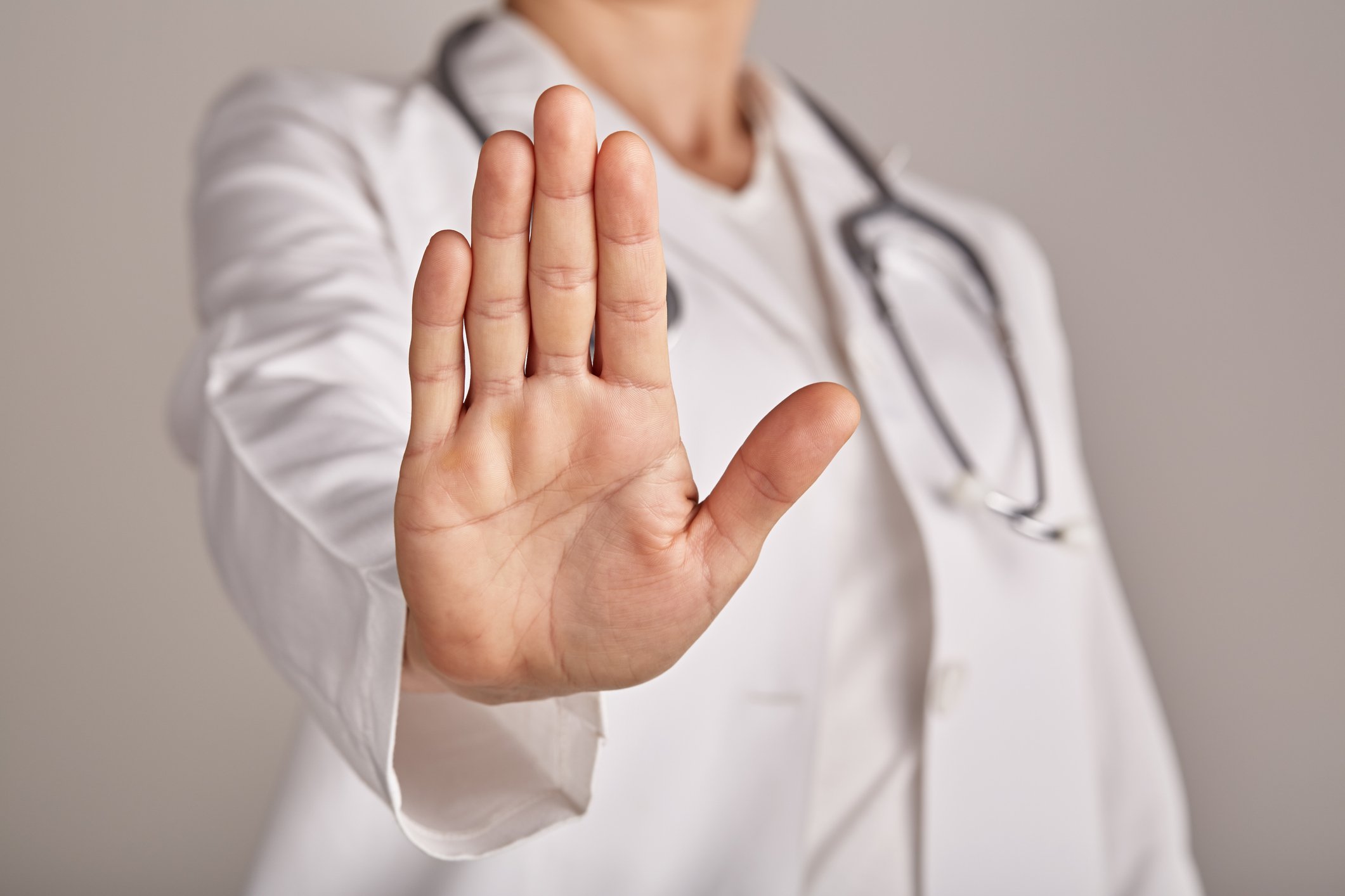 A person wearing a white coat with a stethoscope holding a hand up as if to halt someone.