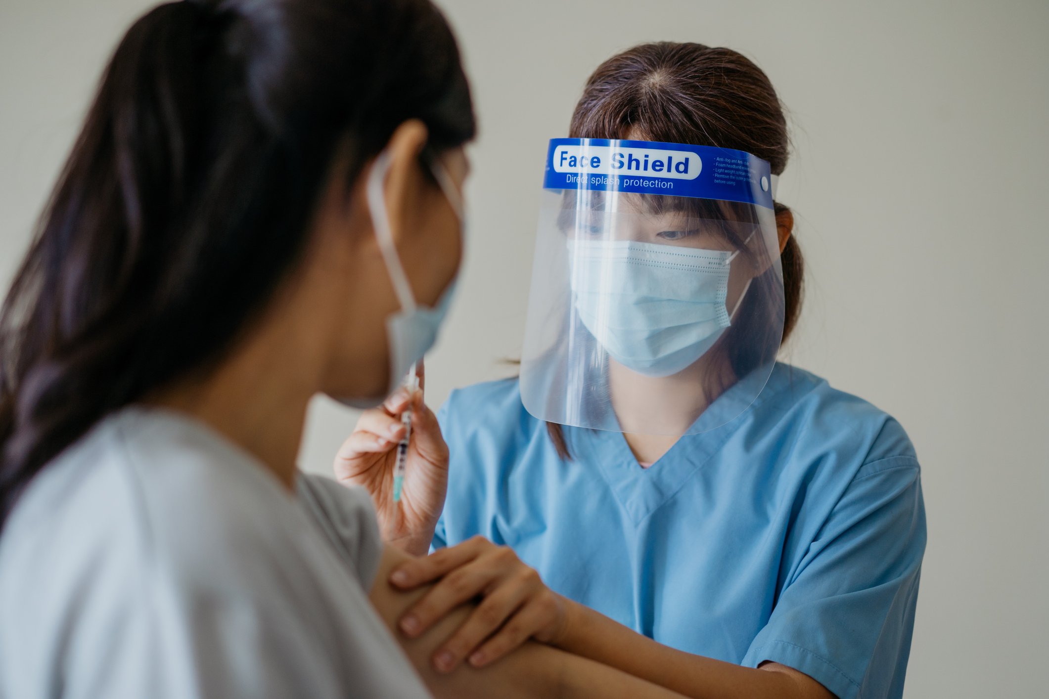 A healthcare professional wearing a face shield giving a vaccine to a person.