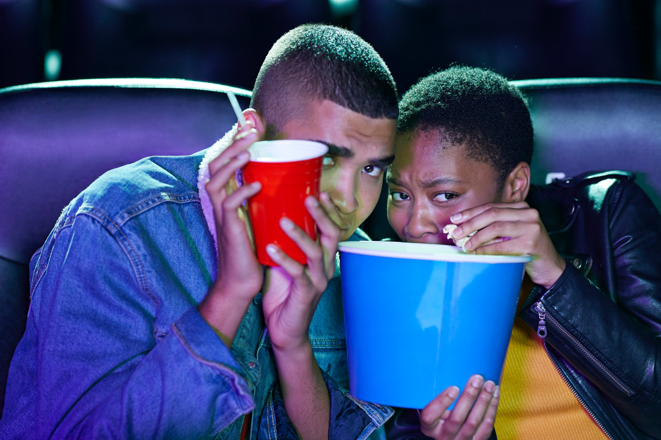 A couple at the movies, scared of a scene, hiding behind their popcorn buckets. 