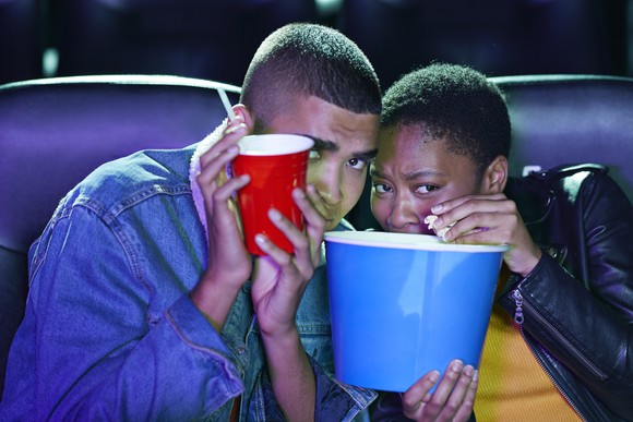 A couple at the movies, scared of a scene, hiding behind their popcorn buckets. 