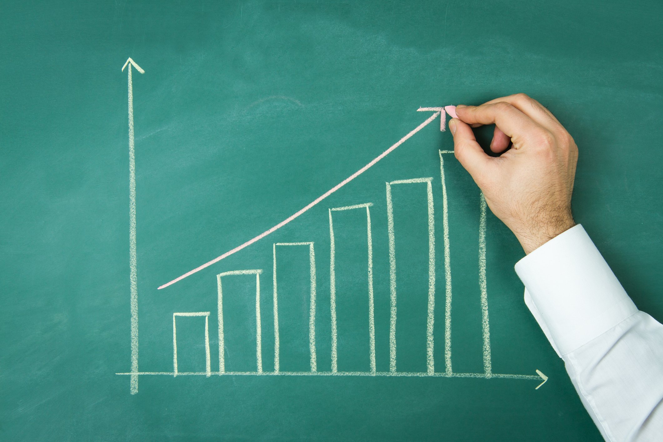Business person plotting a rising bar chart on a chalkboard.