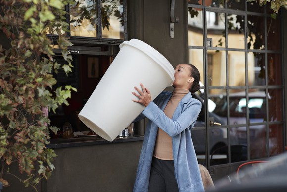 Person drinking a massive cup of coffee outside.