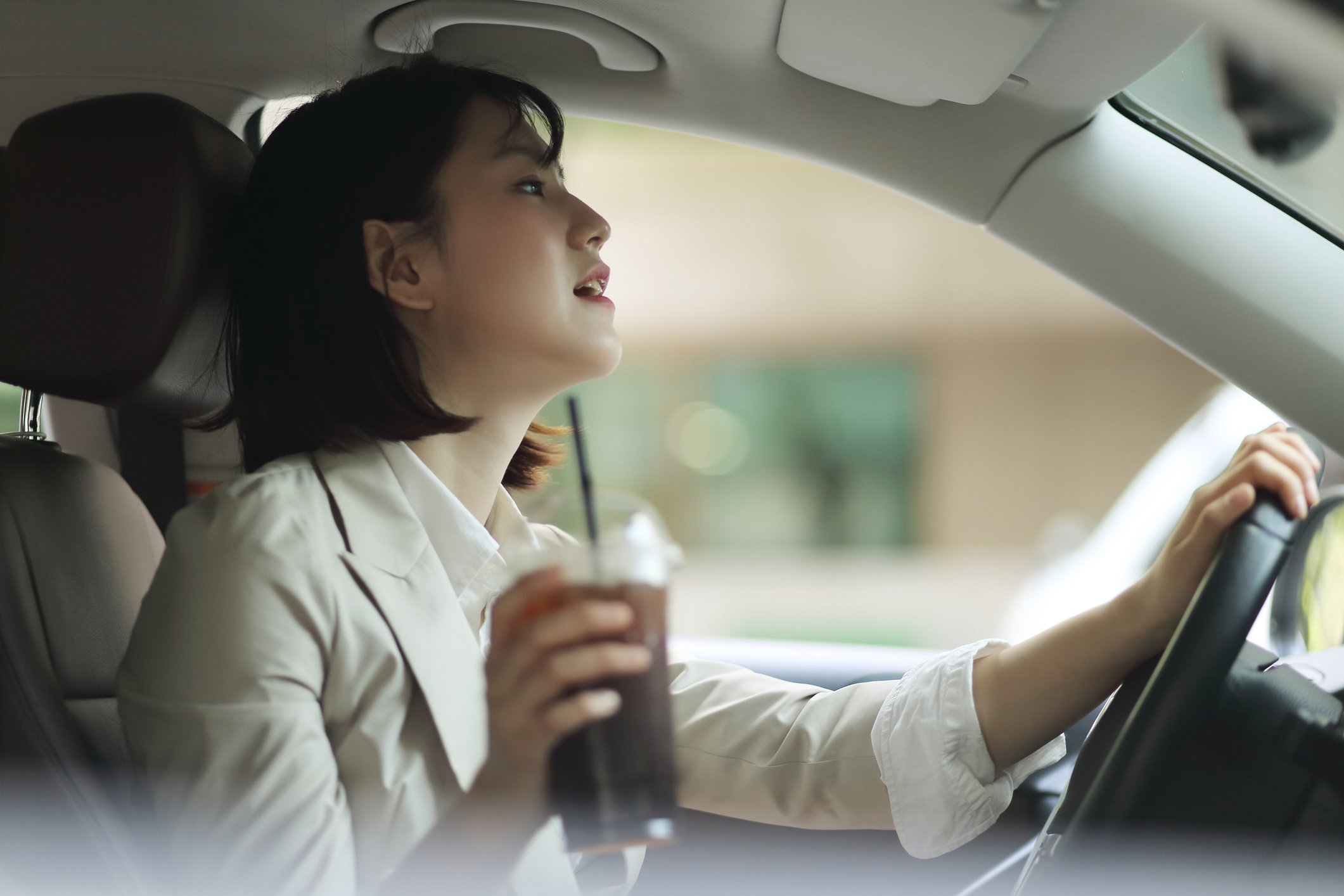 A woman driving with a coffee in hand.