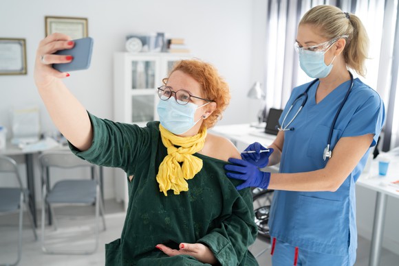A person takes a selfie while receiving the COVID vaccine from a nurse.