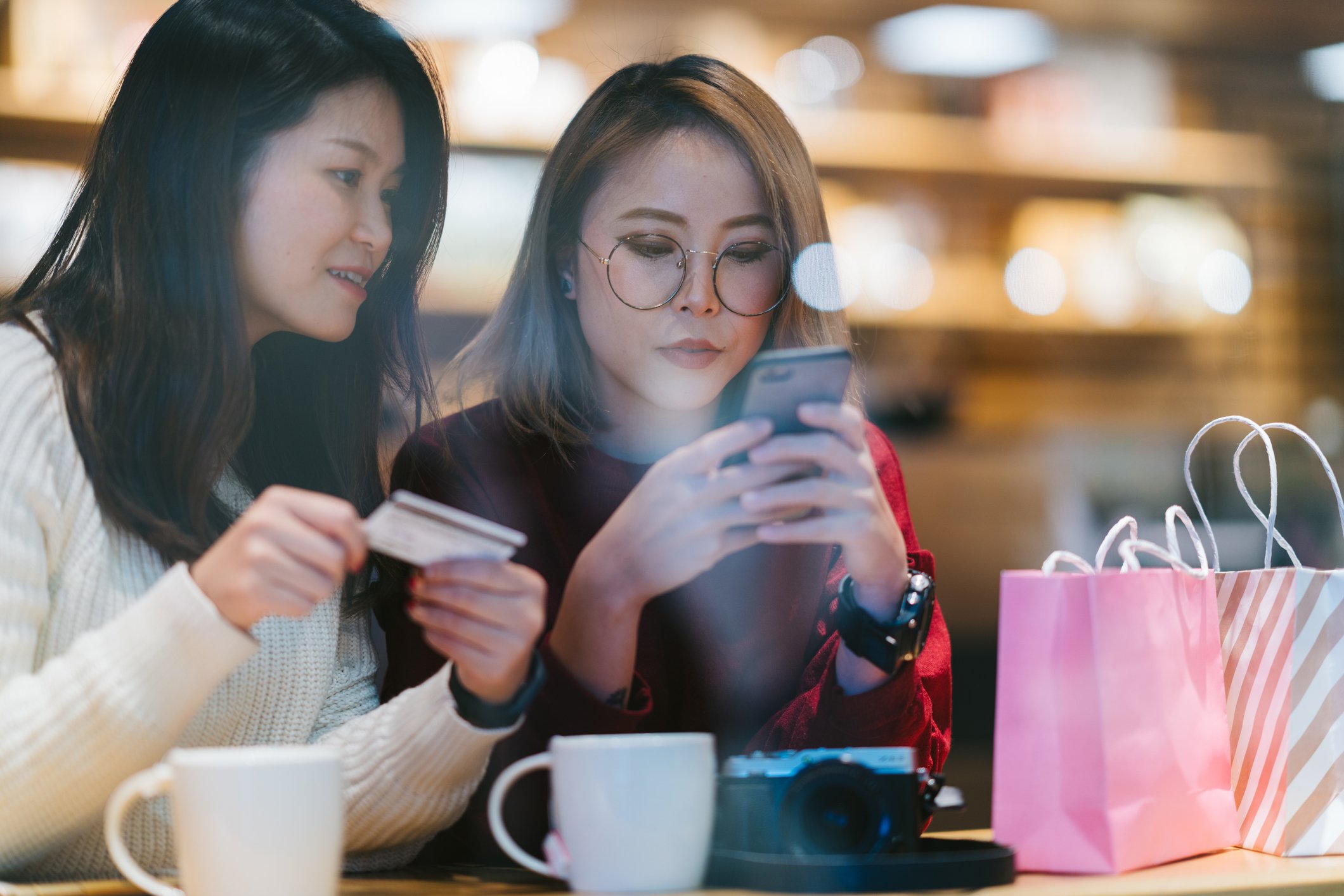 Two young people ordering online. One's holding the phone and the other, a credit card.