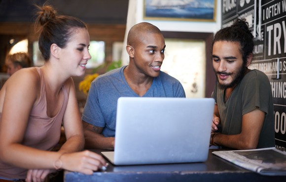 Three people using a laptop in a cafe.