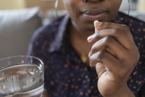 A person holding a glass of water and a pill. 