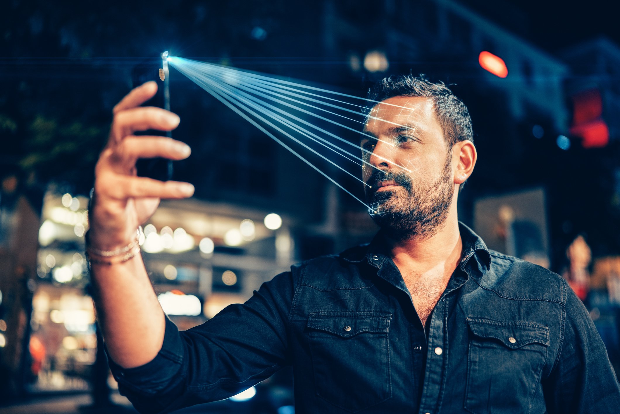 A man uses facial recognition on his phone on a street. 