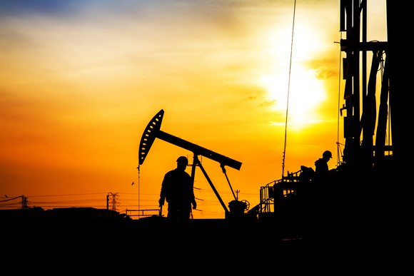 Silhouetted workers on an oil field at sundown.