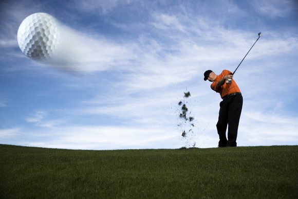 A golf ball whizzing away from a golfer, with a cirrus covered blue sky in the background.