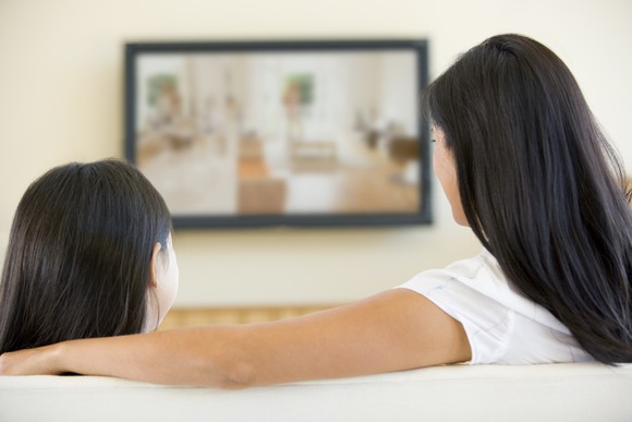 Two people watching a big-screen TV on the couch.