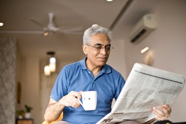 A man hold a mug while reading the newspaper.