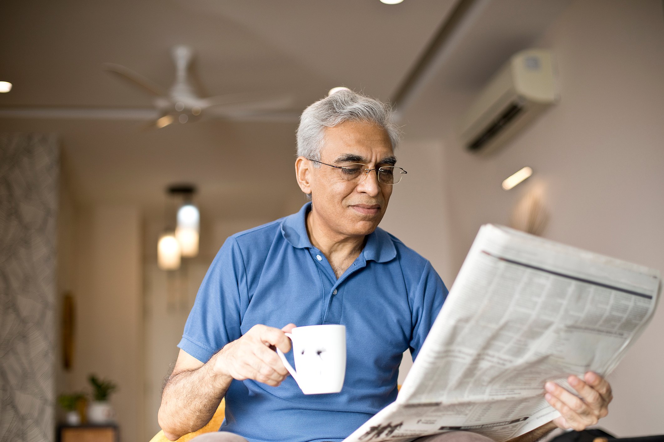 A man hold a mug while reading the newspaper.
