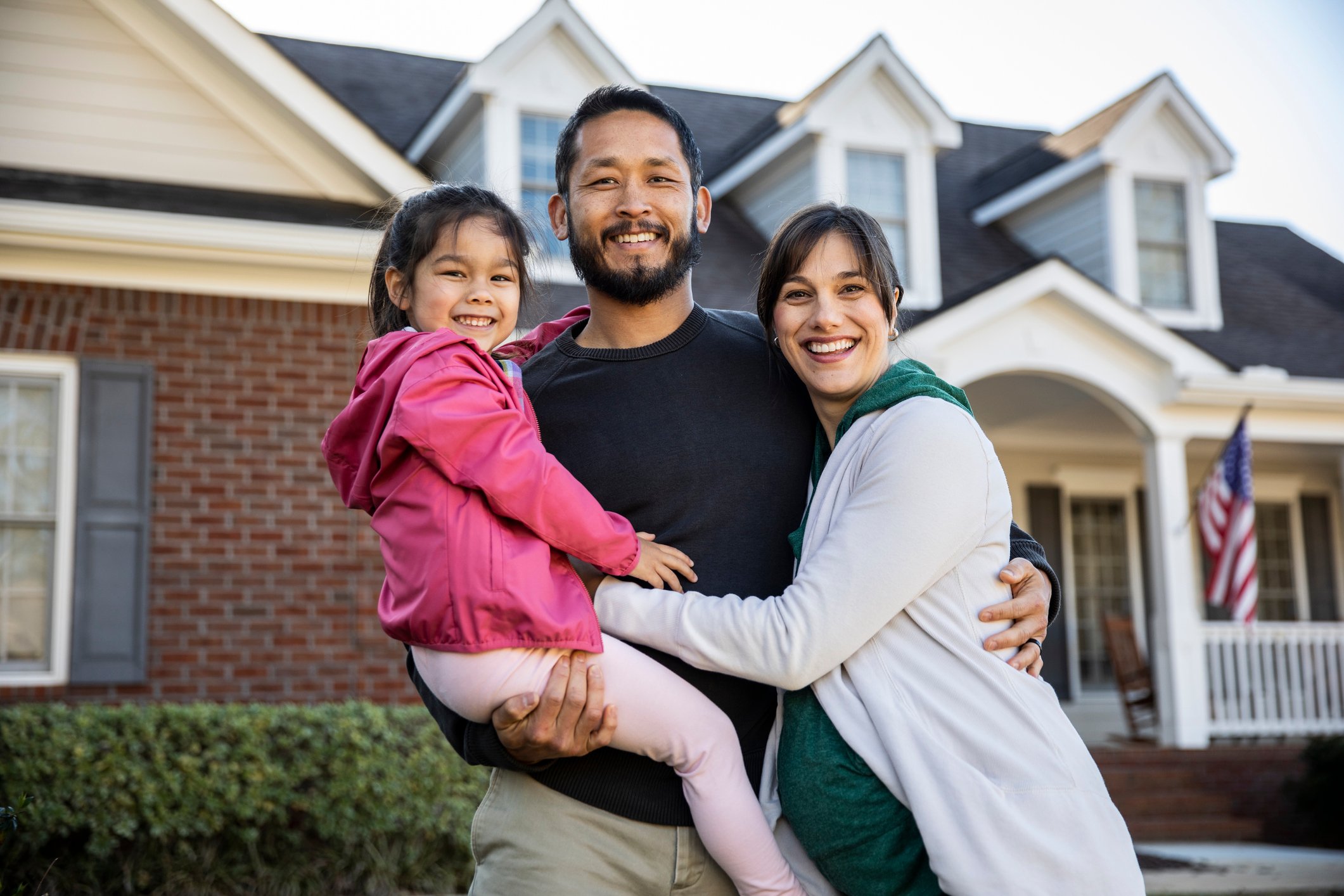 A young family posing in front of a brick house.
