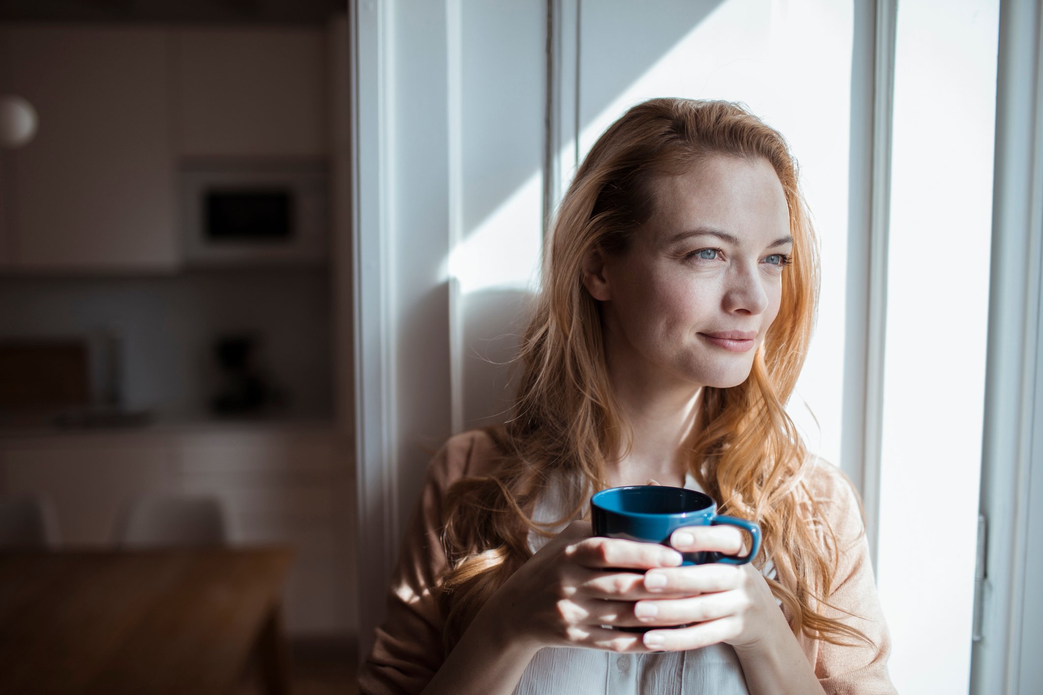 Person holding mug and looking out window.