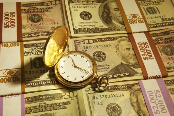 A pocket watch on a pile of cash. 