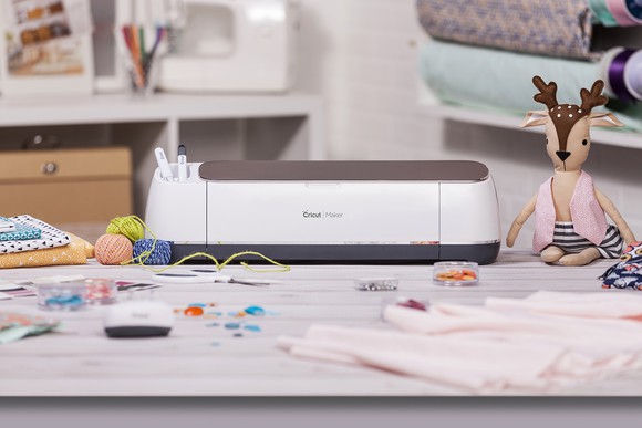 Cricut Maker surrounding by crafting supplies.