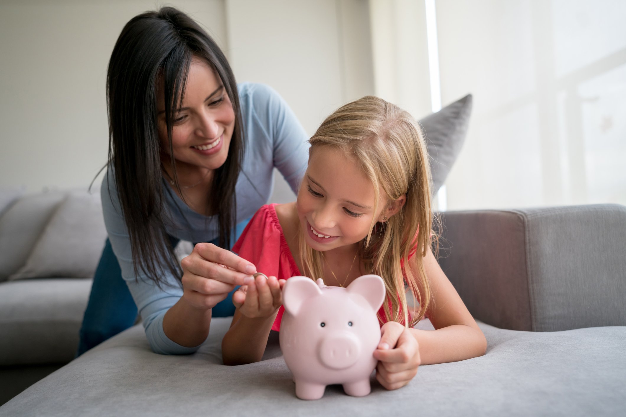 An adult giving a child spare change to put in her piggy bank.