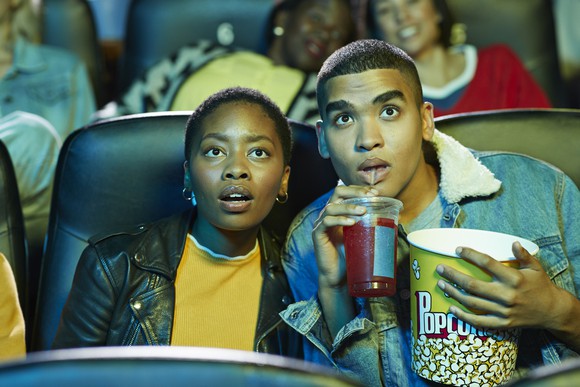 A couple watching a film at a movie theater with popcorn and a beverage.