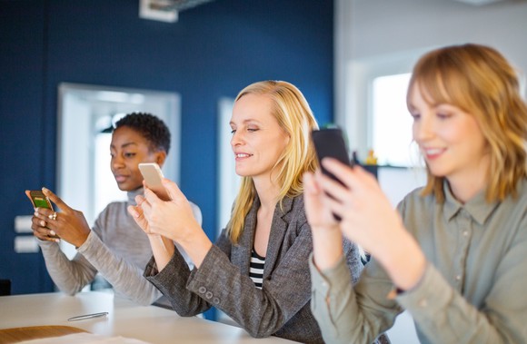 Three smiling people looking at their smartphones.