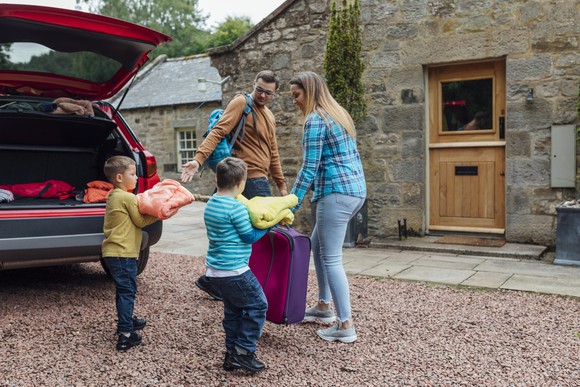 A family arriving at a home with luggage in hand.