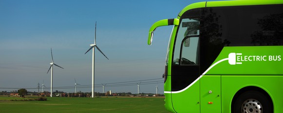 Electric bus driving in front of a wind farm. 