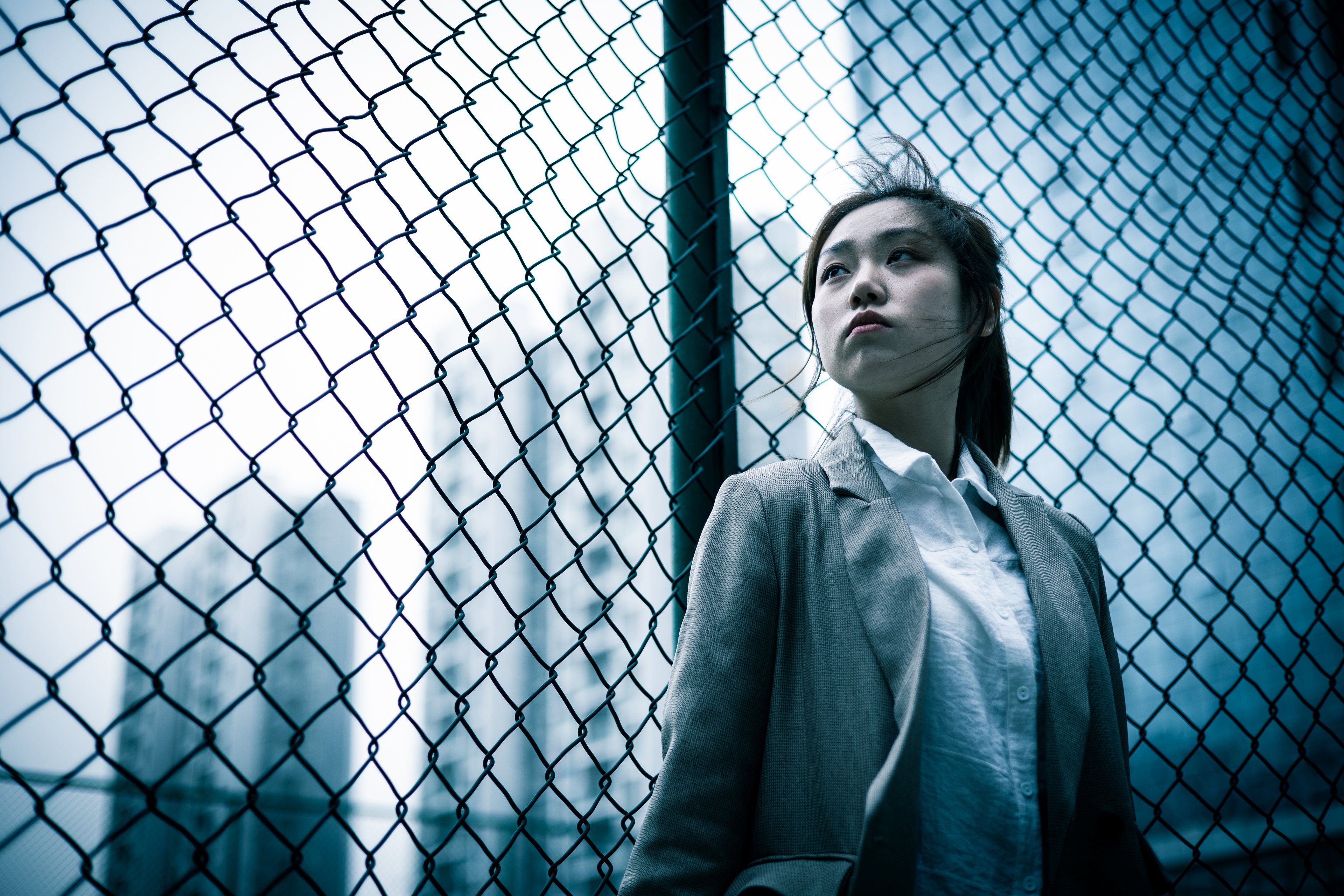 A woman looking uncertain in front of a fence in a high rise complex.. 