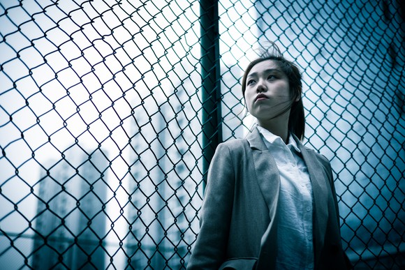 A woman looking uncertain in front of a fence in a high rise complex.. 