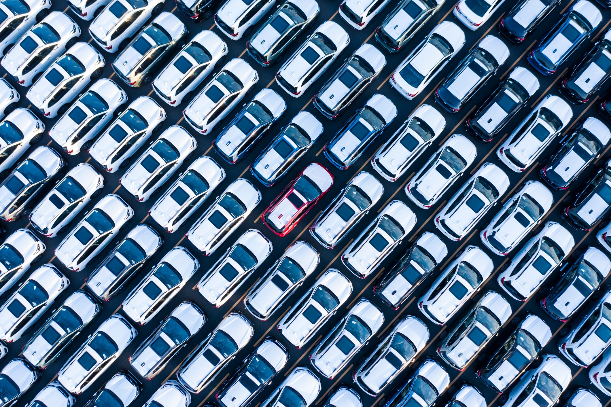 Aerial view of many white cars parked outside a car factory. 