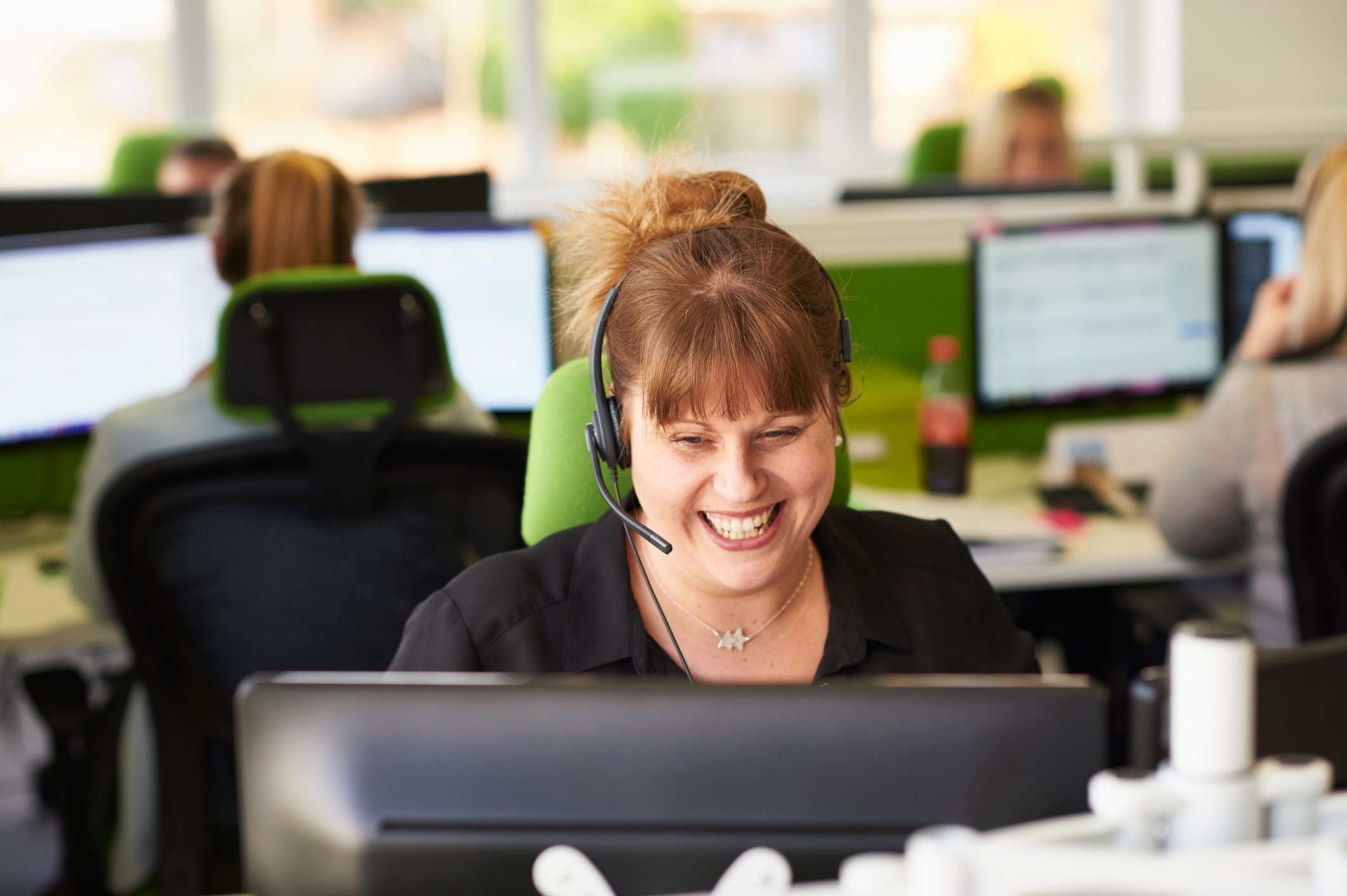 A smiling female customer service rep in front of her desktop in an office. 